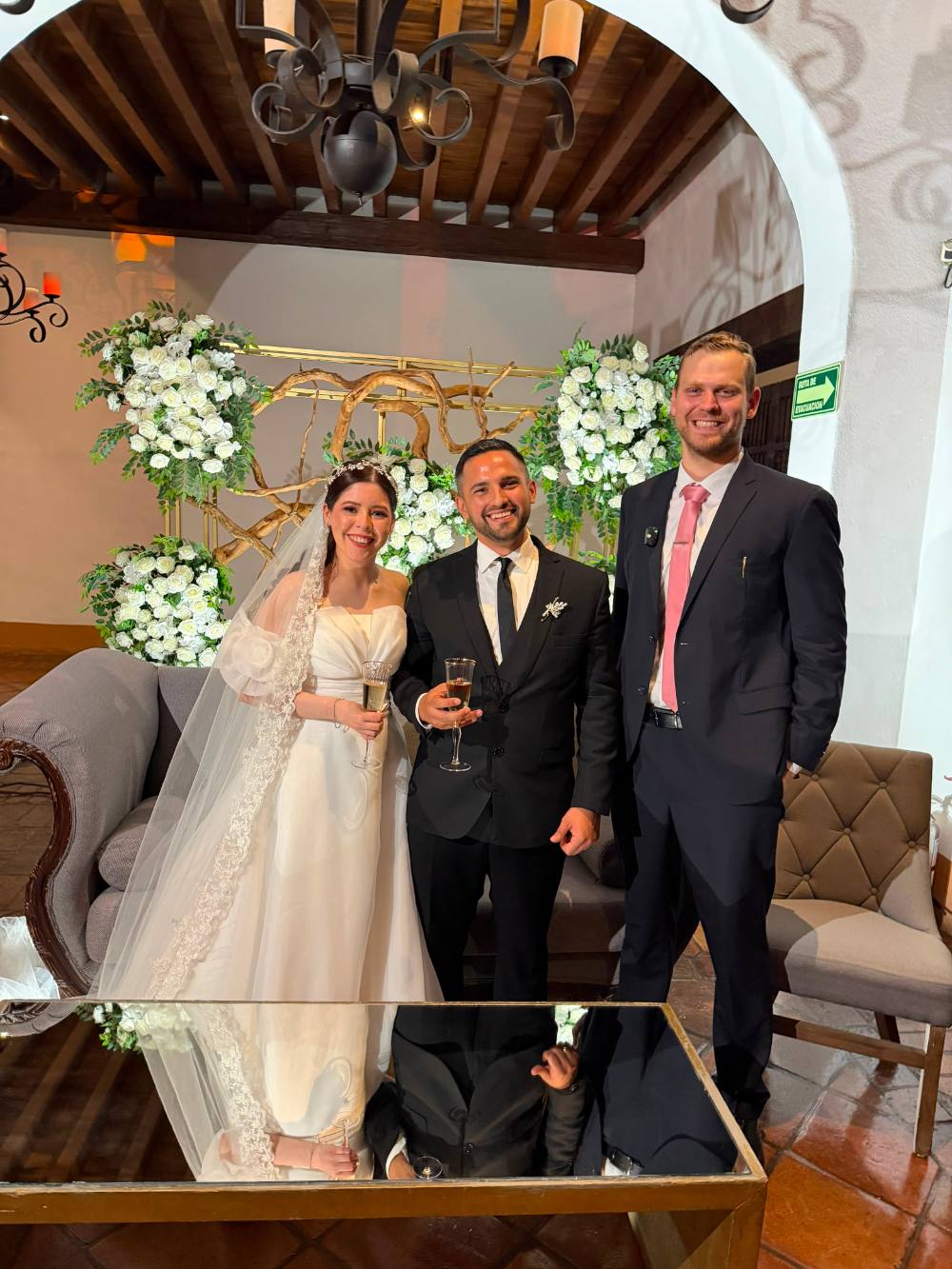 Novios brindando con el juez en un salón decorado con arreglos de flores blancas
