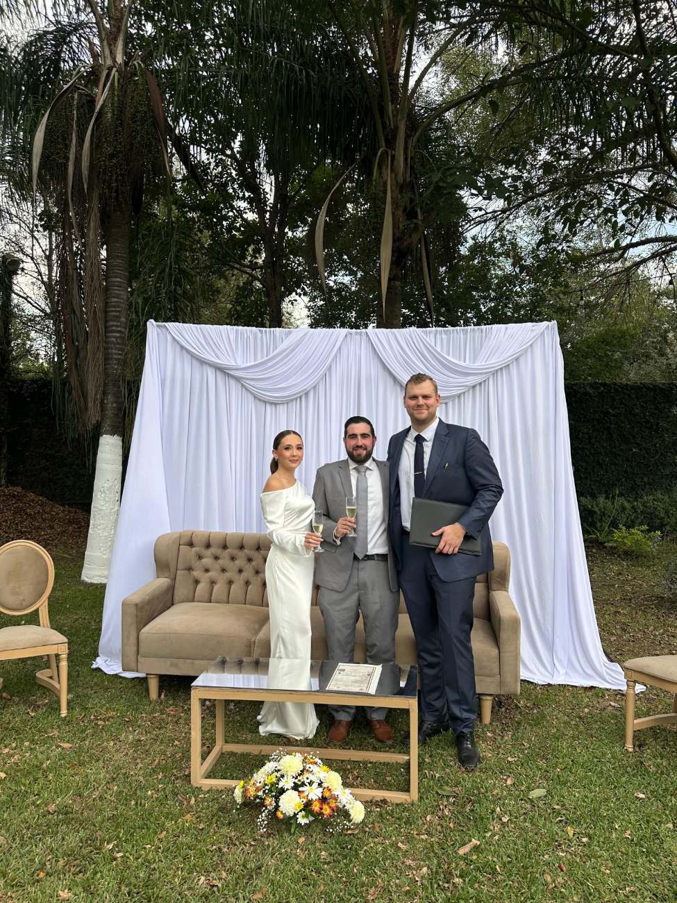 Novios junto al juez en un jardín con cortinaje blanco